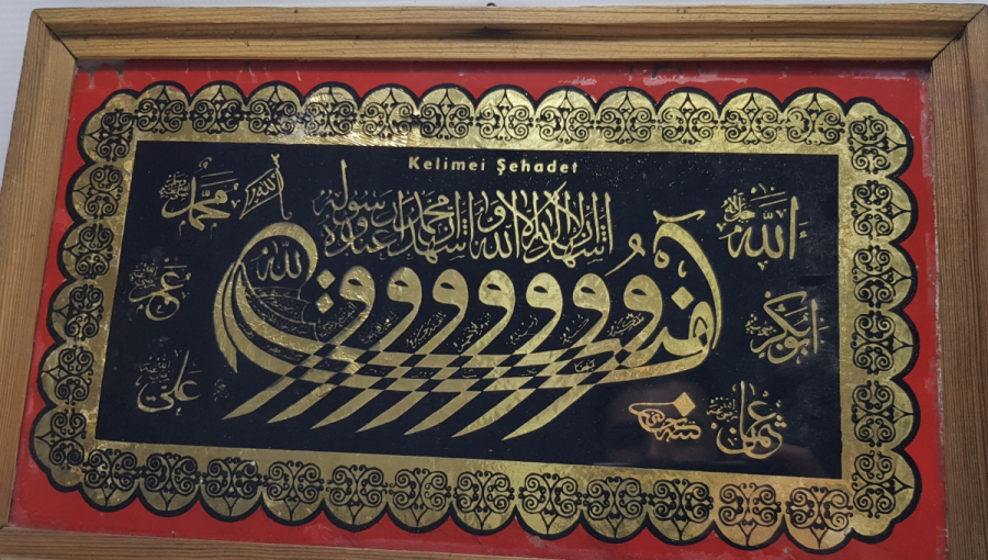 HÜSEYİN KETEBELİ VAV KAYIĞI FORMUNDA KELİME-İ ŞEHADET YAZILI CAM ALTI HAT LEVHA